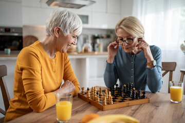 Senior women playing chess and having fun at home