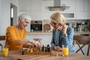 Two senior women playing chess and having fun at home