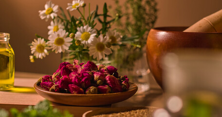 The rose buds dried for longer preservation. The wooden pestle and mortar are used to process the oriental medicine ingredients. The white chrysanthemum branches are placed in a glass jar behind.