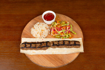 Istanbul kefte, turkish rice with meat with adjika ,mixed salad and local minced meat kebab on a table in a restaurant on a wooden stand