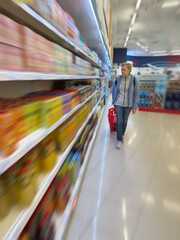 woman with cart walking shopping in supermarket along shelves, blur effect