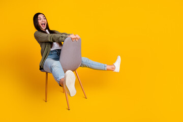 Young woman playfully sitting on a chair with a joyful gesture against a vibrant yellow background