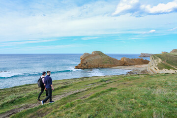 Two people walking through the landscape of the Costa Quebrada in Cantabria