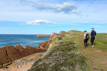 Two people walking through the landscape of the Costa Quebrada in Cantabria
