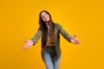 Young stylish woman expressing joy with outstretched arms on vibrant yellow background showcasing...