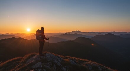 Fototapeta premium A lone hiker stands on a mountain peak, silhouetted against a stunning sunrise, enjoying the view of the expansive landscape.