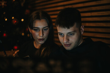 Two individuals sitting closely with intense focus, illuminated by warm, ambient lighting. A...