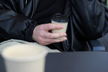 Man hand with coffee to go. Man in black leather jacket in a cafe. Coffee to go in a cafe. Man in...