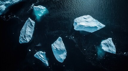 Fototapeta premium Aerial view of icebergs floating in dark waters, showcasing the contrast between the icy formations and the ocean's depths.