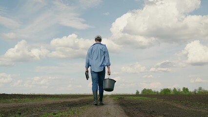 Farmer uses shovel and bucket to grow crop, vegetable field. Farmer businessman works on plowed land with shovel bucket. Concept of harvesting vegetables. Agricultural industry. Agricultural business © Victoriia
