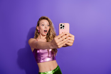 Plakat Stylish young woman captures a surprise moment with her smartphone against a vibrant purple background.