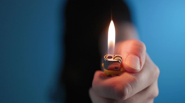 A man holds a lighter and ignites a flame. The fire burns steadily, representing themes of fire, ignition, survival, danger, and warmth