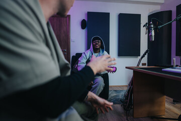 Two multiracial musicians engage in a collaborative session inside a contemporary recording studio. Instruments and microphones create a professional atmosphere.