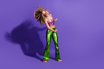 Young woman in stylish retro fashion dancing against vibrant purple background
