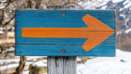 Wooden sign with an orange arrow pointing right, mounted on a post, set against a snowy landscape