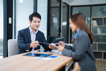 Two asian businesspeople sitting at desk are discussing and working together with documents and financial reports during a meeting in a modern office
