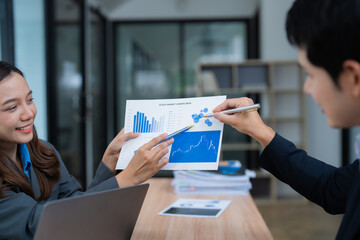 Two business people holding pens are analyzing stock market charts data in an office meeting, discussing financial strategy, investment opportunities and growth potential