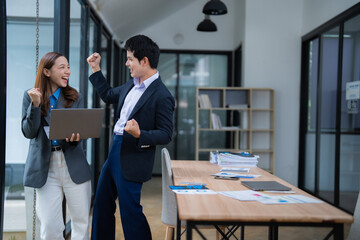 Two happy business colleagues celebrating a successful project while looking at a laptop screen,...