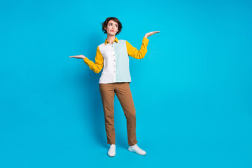 Full length photo of doubtful unsure woman wear shirt showing arms scales looking empty space isolated blue color background