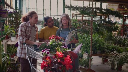 Senior garden center employee explains and advises a young couple choosing plants and flowers, helping them read the instructions on a fertilizer bag - Powered by Adobe