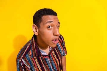 Trendy young man with a stylish colorful shirt winking expressively against a vibrant yellow...