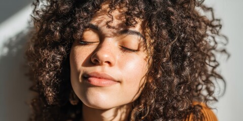 Young woman with curly hair enjoying sunlight in a cozy indoor setting during the afternoon