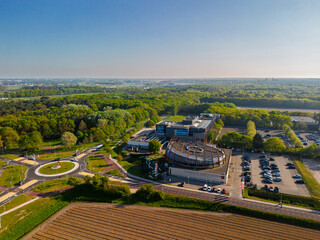 Aerial view of a rural area with a large building complex surrounded by farmland, green forests, a...