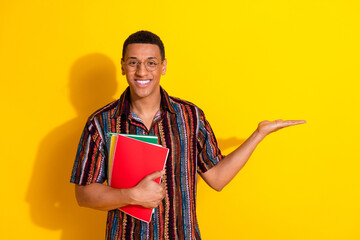 Vibrant young man holding notebooks gestures confidently against a vibrant yellow background