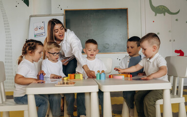 Smiling, learning, playing game by table. Children in kindergarten with their teacher