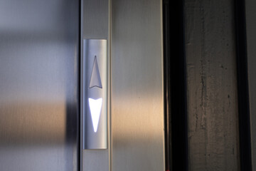 Close-up of a sleek, illuminated up arrow button on a stainless steel elevator panel. Modern design.