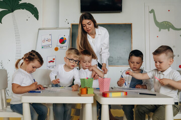Holding markers, learning to draw. Children in kindergarten with their teacher