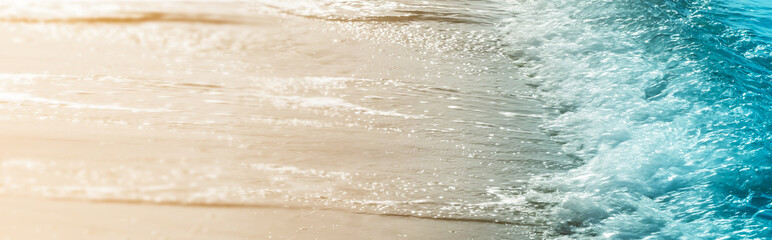 closeup of a real blue water wave at sand beach in glittering sunlight, summer nature idyll, blurred background banner concept with copy space for vacation, travel and relaxation outdoors
