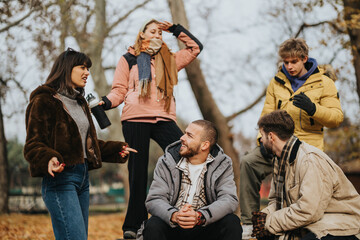 A group of young friends having a fun and relaxed conversation outdoors during autumn. They are...