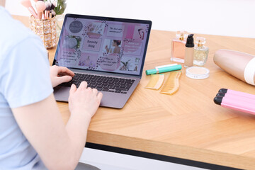 Blogger using laptop with beauty blog web site at wooden table indoors, closeup