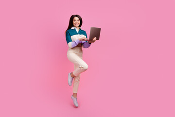Charming Young woman with laptop jumping on pink background showing happy and trendy style