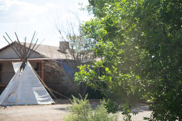 Stock photo of a teepee and a rustic house in a sunny landscape with green trees. Perfect for travel, adventure, and nature themes. © vegefox.com