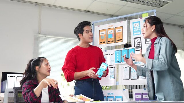 Creative team reviewing and discussing mobile app design in modern office environment, sharing ideas and collaborating on user interface and user experience