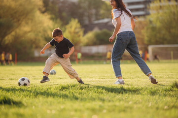 Obraz premium Active time spending with soccer ball. Mother and son are together on the summer field