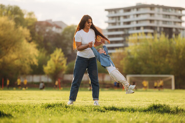 Cheerful, having fun, holding boy in hands. Mother and son are together on the summer field