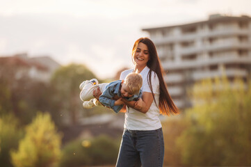Cheerful, having fun, holding boy in hands. Mother and son are together on the summer field