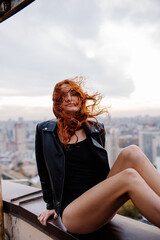 Red-haired girl in shorts and a leather jacket on a rooftop