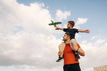 Against cloudy sky, with toy plane. Father and son are having fun outdoors
