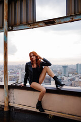 Red-haired girl in shorts and a leather jacket on a rooftop