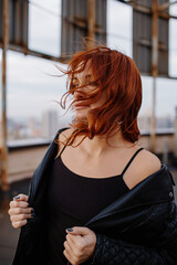 Red-haired girl in shorts and a leather jacket on a rooftop