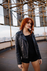 Red-haired girl in shorts and a leather jacket on a rooftop