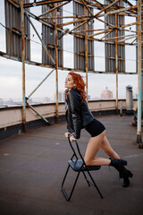 Red-haired girl in shorts and a leather jacket on a rooftop