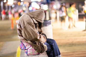 Obraz premium A poignant photo depicting a homeless woman sitting alone at night, conveying feelings of loneliness and despair. Ideal for articles about homelessness and