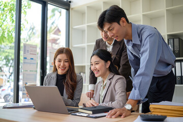 Group of young business professionals collaborating and discussing ideas together around a laptop in a modern office.
