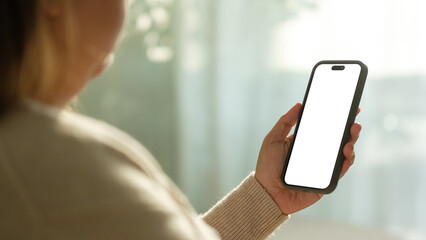 Hands holding a smartphone with white blank screen in natural light, for mockup or UI design presentations.