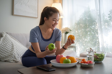 Smiling woman picking up a fresh orange from a bowl, ready to enjoy a healthy snack in her living...